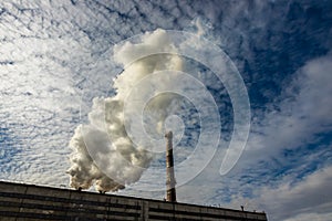 White and gray smoke and steam from a high concrete chimney against the bright blue sky