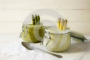 White and green asparagus cream soup in glass jars against a bri