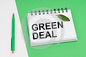 On a white-green background lies a pen, a leaf of a plant and a notepad with the inscription - Green Deal