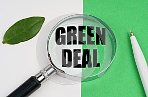 On a white-green background, a pen, a piece of paper and a magnifying glass with the inscription - Green Deal