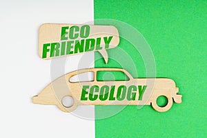 On a white and green background, a wooden figure of a car - Ecology and a sign with the inscription - ECO FRIENDLY