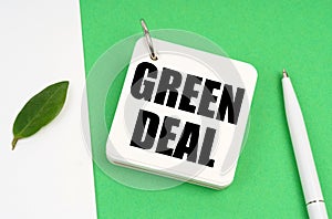 On a white-green surface, a piece of paper, a pen and a notepad with the text - Green Deal