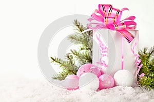 White greeting card with copy space for christmas or new year with a wrapped gift, fir branches and pink ball on snow