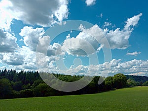 White and grey clouds on a blue sky in front of forest in german region Eifel