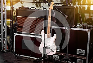 White guitar on stage among amplifiers and other musical equipment.