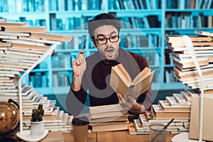 White guy surrounded by books in library. Student is emotionally reading book.