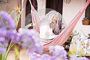 White hair diversity senior woman relax on an hammock in the garden at home reading a paper book and enjoying the quaity of