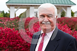 White Hair Senior Businessman Outside by the Red Burning Bushes