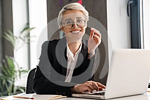 White-haired joyful woman working with laptop while sitting at table