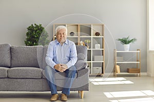 White-haired senior man sitting alone on couch at home and thinking about his life