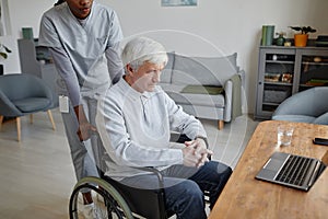 White haired senior man in wheelchair at home with nurse assisting