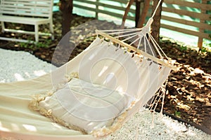 White hammock and pillow for relaxation in the backyard garden shade on a summer afternoon. Comfortable hammock with pillow hangin