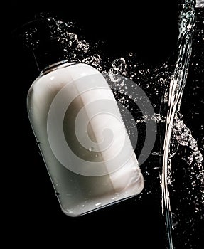 White hand cream bottle splashing with water droplets on the black background