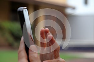 White hand manipulates smartphone against blurred garden background