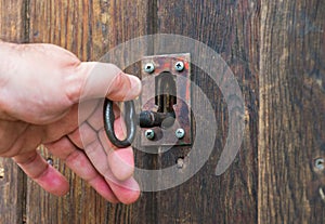 white hand moving an old or vintage key made by metallic iron inside a lock of a wooden door. The old key and the lock are