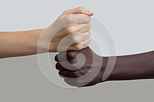 A white hand in the shape of a fist, lying on top of a dark-skinned fist. Gray isolated background, selective focus. The concept