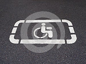 White handicapped symbol of wheelchair painted on asphalt on a parking lot, sign of parking space for disabled visitors