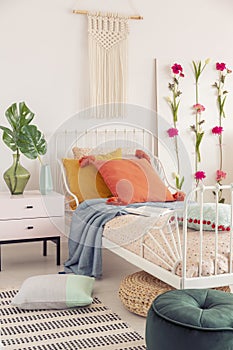 White handmade macrame above above single metal bed with colorful pillows and patterned duvet, real photo