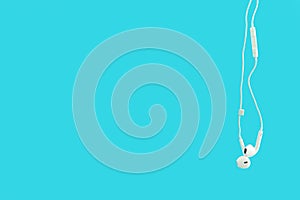 White hanging ear buds headphones isolated on a blue