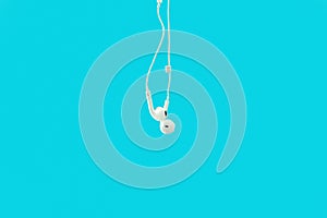 White hanging ear buds headphones isolated on a blue