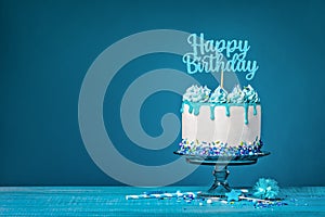 White happy birthday cake with teal ganache over a blue background