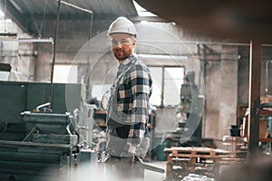 In white hard hat. Factory male worker in uniform is indoors