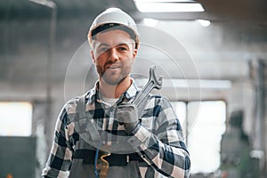 In white hard hat. Factory male worker in uniform is indoors