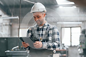 In white hard hat. Factory male worker in uniform is indoors