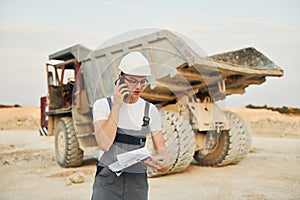 In white hard hat. Worker in professional uniform is on the borrow pit at daytime