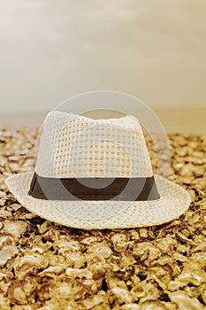 A white hat with a black ribbon lies on a shell beach on a blurred background of sky and sea