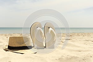 Hat and white flip-flops on the beach with blue sea in the background