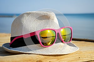 White hat on a wooden pier with fashionable pink sunglasses and reflection