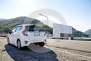 White hatchback car parking on roadside with white billboard against green mountain