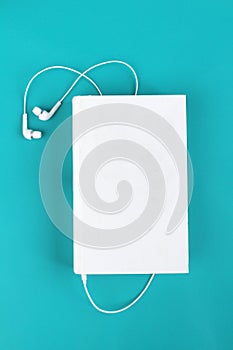 White headphones and book. Isolated on blue background with space for text. Concept to listen to audio books