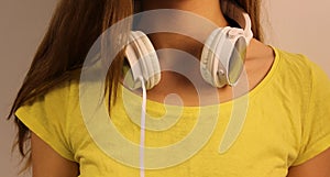 White headphones close-up hanging on the neck of the young girl in a yellow T-shirt