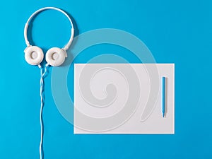 White headphones, a white piece of paper and a blue marker on a blue background.