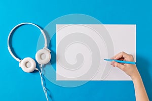 White headphones, a piece of paper and a hand with a marker on a blue background.