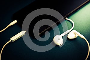 White headphones plug in smart phone , Isolated on a shiny black background , Drak green