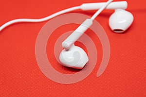 White headphones on a red background, earbuds closeup