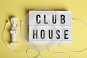 White headphones with small statue and lightbox with text clubhouse on yellow background