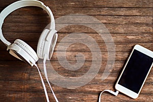 White headphones and smartphone on timber background. Hipster devices for music listening or entertainment.