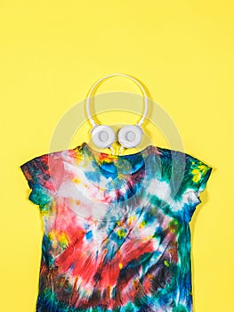 White headphones and a tie dye t-shirt on a yellow background. Flat lay.