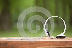 White headphones on wooden table at the background of nature