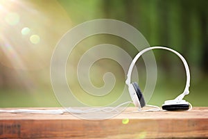 White headphones on wooden table at the background of nature