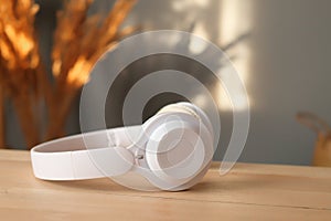 White headphones on wooden table and bouquet of dry flowers over gray house wall with sunlight shadows copy space advertisement