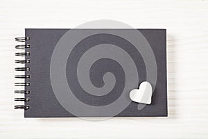 White heart on a black notebook, top view, isolated and copy space, on a white wooden background.