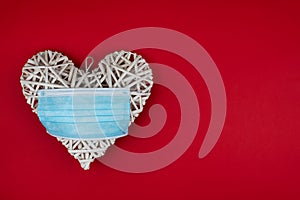 White heart with a blue face mask on a red background. Concept of a ValentineÂ´s day during Coronavirus or Covid pandemic