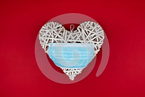 White heart with a blue face mask on a red background. Concept of a Valentines day during Coronavirus or Covid pandemic