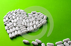 white heart made of pills on a green background.