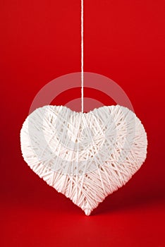 White heart made of wool on a red background.